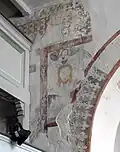 Detail stěny u vítězného oblouku s freskami, na nich ozdobné rámečky a osoba držící plátno s otiskem obličeje Ježíše Krista.