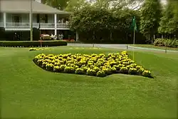 Obrys mapy USA, vysázený ze žlutých květin, na trávníku. V místě města Augusta je v mapě zabodnuta golfová praporková tyč.