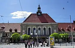 Barevná fotografie s budovou nádraží a stromy