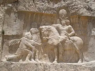 Císař Valerianus poklekávající před velkokrálem Šápúrem I., sedícím na koni, skalní reléf v Nakš-e Rustamu
