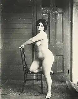 Storyville prostitute, stojící nahá žena opírající se kolenem o židli, 1912
