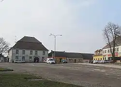 Podlouhlá, k jihu se rozšiřující náves s domem č.p. 213 (hostinec), sochou sv. Jana Nepomuckého a radnicí