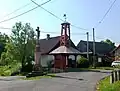 Kamenný kříž z roku 1910 a dřevěná zvonice se zvonem sv. Barbory z r. 1703