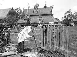 Šaman kmene Karo-Batak provádí rituály s hůlkou, vajíčkem a chameleonem při obřadu ve vesnici „Kabanjahe“ na Sumatře, v pozadí dům Pa Mbelgaha