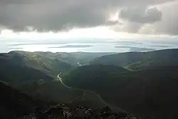 Pohled do zelenošedého údolí s prudkými srázy, vzadu rozsáhlá vodní plocha