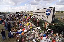 Skupina lidí přinášející květiny a různé předměty před areál NASA