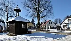 Dřevíkovská náves s dřevěnou zvoničkou, vlevo pomník obětem válek, pod lípou Boží muka, vpravo rodný dům Františka Hrnčíře