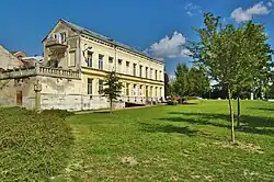 Pohled od muzea na vysokou dvoupodlažní budovu se žlutou fasádou ve Smyčkově ulici v Litovli. Vpředu k budově přiléhá nízká oprýskaná přístavba s terasou a kamenným zábradlím na střeše.