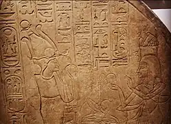 Kamenná stéla pokrytá hieroglyfy a ukazující dvě stojící postavy, vlevo stojí bůh Osiris, vpravo žena, která mu nabízí kadidlo