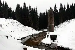 Protržené těleso přehrady, jímž protékají vody Bílé Desné a stojí zde šoupátková věž. Celá krajina je zasněžená.