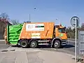 Popelářský vůz s nástavbou pro lineární lisování. Lis je umístěn v zelené části nástavby