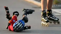 Pád jako důsledek labilní rovnovážné polohy člověka na kolečkových bruslích.