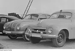 černobílá fotografie přední části sanitního vozu Škoda 1200. Za ním stojí vůz Tatra 600.
