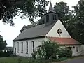 Barevná fotografie s pohledem na nevelkou stavbu na obdélníkovém půdoryse se sanktusníkem