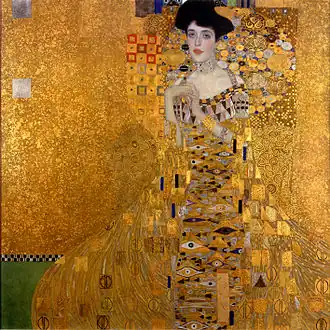 Obraz elegantní ženy s tmavými vlasy a černým kloboukem, stojící na zlatém pozadí. Je oblečená v bohatě zdobených šatech s geometrickými vzory a ornamenty v převážně zlatých, modrých a červených tónech. Celá kompozice je charakteristická Klimtovým osobitým stylem secese s použitím reálných zlatých plátků, rozmanitých ornamentů a geometrických vzorů. Pozadí i šaty splývají v jednu dekorativní plochu, kde figurální prvky přecházejí do abstraktních.