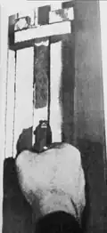 „Zákulisí“ výškoměru. Dole ruka kata s nabitou pistolí a hlavní prostrčenou štěrbinou (pohled ze strany popravčího)