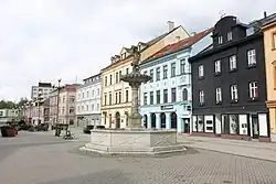 Celkový pohled na kašnu se sokolníkem a budovy lemující pravou stranu Starého náměstí.