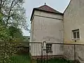 Snížená věž se zřetelným místem nedochovaného nápisu. Zeď navazující na věž (v pozadí) je pozůstatkem původní jižní stěny modlitebny.