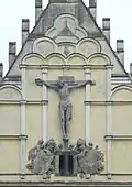 Západní průčelí kostela svatého Bartoloměje v Pardubicích, detail. Štuková výzdoba: Boží oko, Ukřižovaný, erby rodu Pernštejnů a města Pardubic, 1913