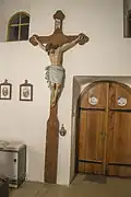 Barevná fotografie vysokého dřevěného kříže, který stojí v interiéru kostela po levé straně vchodu.