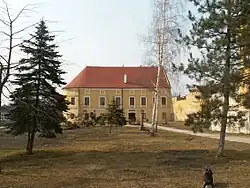 V pozadí budova muzea, před níž se nachází malý parčík s několika stromy a s božími mukami.