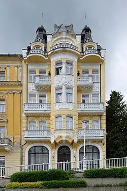 Pětipodlažní dům se žlutou omítkou doplněnou bílými detaily.