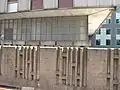 Spodek východní části s hliníkovými dveřmi, okny, betonovými truhlíky a betonovým plotem s reliéfem
