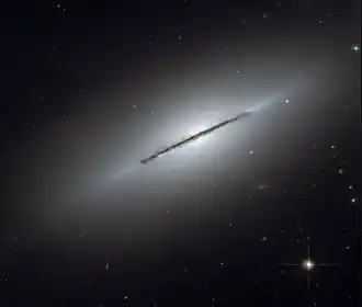 Snímek Vřetenové galaxie, která je k Zemi natočena svou hranou a podél této hrany je vidět dlouhý tmavý prachový pás