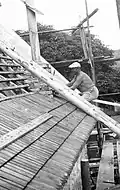 Černobílá fotografie kostela během opravy v roce 1966, pohled na dělníka opravujícího střechu