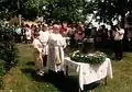 Barevná fotografie slavnostního posvěcování zvonu v roce 1996, v popředí je farář se zvonem na stole, v pozadí lidé