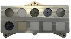 Řada malých kousků různých materiálů tvořících desku s kruhovými výřezy.