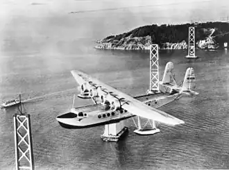Sikorsky S-42 společnosti Pan American Airways letící nad rozestavěným mostem Bay Bridge