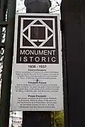Trojjazyčná cedule na hlavní bráně v krátkosti popisuje historii budovy.