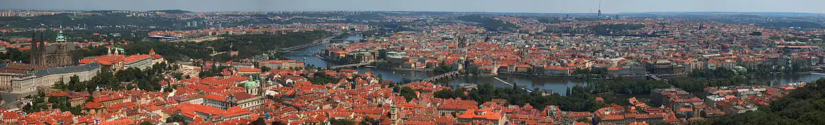 Panorama Prahy z Petřínské rozhledny. Vlevo jsou vidět Hradčany s Pražským hradem, jemuž dominuje svatovítská katedrála, pod nimi se rozkládá Malá Strana s chrámem sv. Mikuláše a věží Pražského Jezulátka. Ve středu snímku záhyb Vltavy překlenutý (zprava) Karlovým, Mánesovým a Čechovým mostem obtéká Staré Město. U horizontu leží Severní Město, Letná a Holešovice, Karlín, Vinohrady, Nové Město, Žižkov, Pankrác, Podolí i další čtvrti a Žižkovský vysílač.