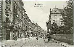 Pohled do ulice. Ve vydlážděné vozovce jsou patrné tramvajové koleje.