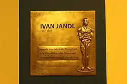 Pozlacená pamětní deska, v jejíž pravé části je silueta Oscara a vpravo nápis „Ivan Jandl 1937–1987. Historicky první český držitel filmových cen Oscar a Zlatý Glóbus za film Poznamenaní. Svá nejlepší tvůrčí léta prožil v Divadle Gong. V roce 2014 mu bylo uděleno čestné občanství Prahy 9.“