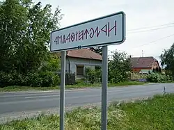 Cedule u vjezdu do Rákóczifalvy s názvem města psaným v rovasu