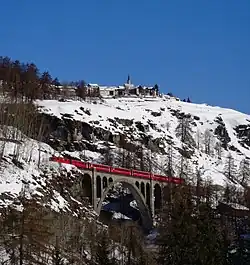 Vlak na viaduktu Tuoi s obcí Guarda v pozadí