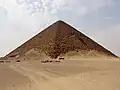 Pohled na pyramidu zdálky, poblíž které stojí nákladní automobil. Pyramida má tmavě béžovou barvu.