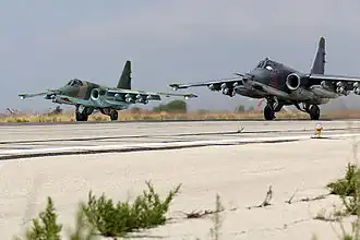 Dva Suchoje Su-25SM se 3. října 2015 chystají ke startu na letišti Chumajnim (vojenská část mezinárodního letiště Básila al-Asada) v Latákii. Každý stroj má vedle přídavných nádrží podvěšeny čtyři tříštivo-trhavé pumy OFAB 250/270