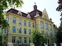 Zdobená třípodlažní žlutě omítnutá budova. Na střeše se nad vchodem nachází věžička. Před budovou se nachází kovový plot se zděnou podezdívkou a sloupky.