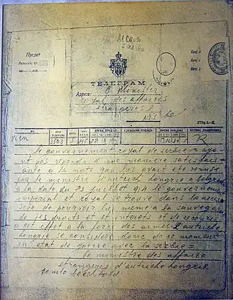 Fotografie ukazuje historický telegram, formulář vyplněný ručně psaným textem. Telegram má razítka a tištěné texty v cyrilici, zatímco adresa a text zprávy je v latince a psán francouzsky.
