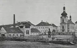 Historická fotografie náměstí s později zbořeným panským lihovarem; vpravo zámek a kostel