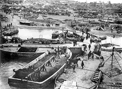 Vyloďování dohodových sil na poloostrově Gallipoli. V popředí čluny z nichž jsou na břeh vyváděni koně. V pozadí tábor hemžící se vojáky.