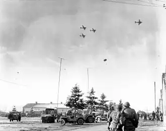 Příslušníci 101. americké výsadkové divize sledují letouny C-47 shazující zásoby pro obležené výsadkáře